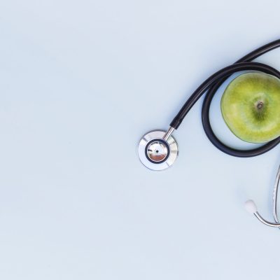 elevated-view-stethoscope-around-green-apple-blue-background